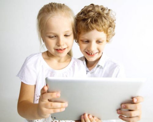 Boy and girl in jeans, best friends or brother and sister having fun. Making a selfie on tablet on white studio background. Childhood, education, holidays or homework concept, modern technologies.